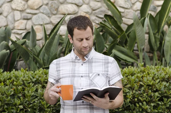 Adam bir turuncu kahve kupa tutarken İncil okuma.