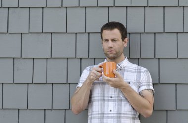 Bir turuncu kahve fincanı gri bir arka plan ile iki elle tutan adam.