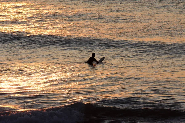 Silhouet van een eenzame surfer die wachten op een golf in de buurt van het strand bij zonsondergang — Stockfoto