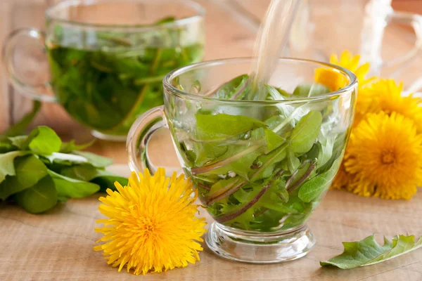 Löwenzahntee zubereiten, indem man heißes Wasser über frische Löwenzahnblätter gießt — Stockfoto