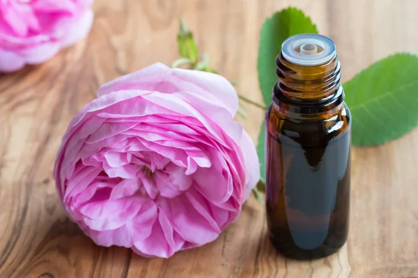 Una bottiglia di olio essenziale di rosa con fiori di rosa sullo sfondo — Foto Stock