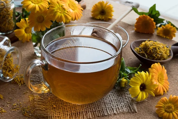 En kop calendula te med calendula blomster i baggrunden - Stock-foto
