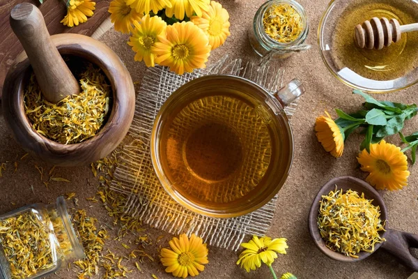 Una taza de té de caléndula con flores de caléndula en el fondo — Foto de Stock