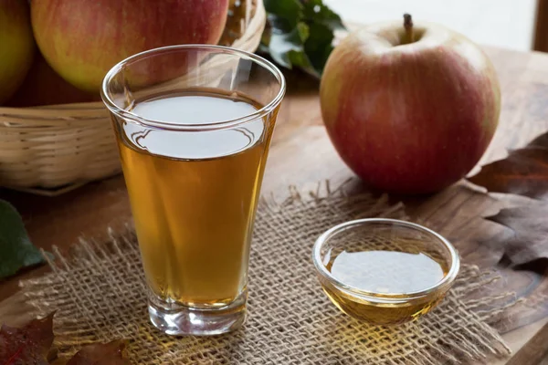 Äppelcidervinäger i ett glas, med äpplen i bakgrunden — Stockfoto