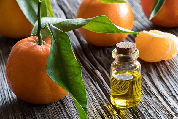 A bottle of tangerine essential oil with tangerines in the backg