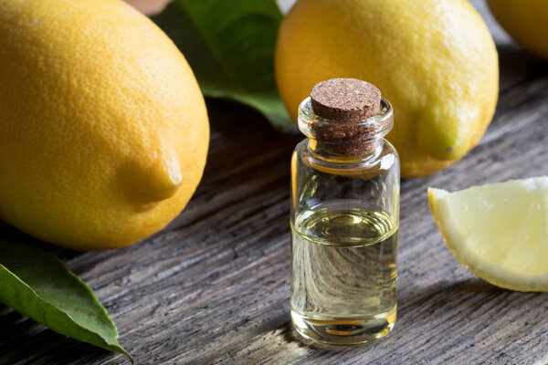 A bottle of lemon essential oil with lemons in the background