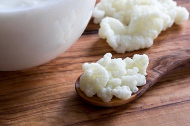 Kefir taneleri üzerinde bir tahta kaşık yanında bir bardak süt