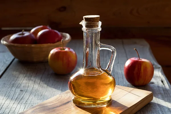 Una botella de vinagre de manzana con manzanas en el fondo — Foto de Stock