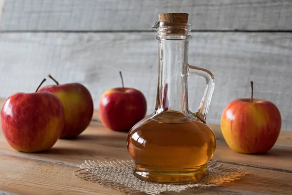 Una botella de vinagre de manzana con manzanas en el fondo — Foto de Stock