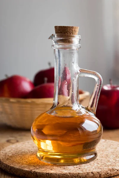 Eine Flasche Apfelessig mit roten Äpfeln im Hintergrund — Stockfoto