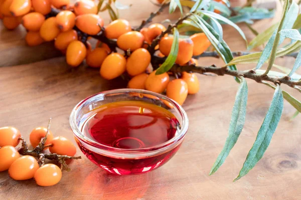 Olio di olivello spinoso in una ciotola di vetro con ramo di olivello spinoso fresco — Foto Stock