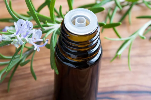 Una bottiglia di olio essenziale di rosmarino con ramoscelli di rosmarino in fiore — Foto Stock