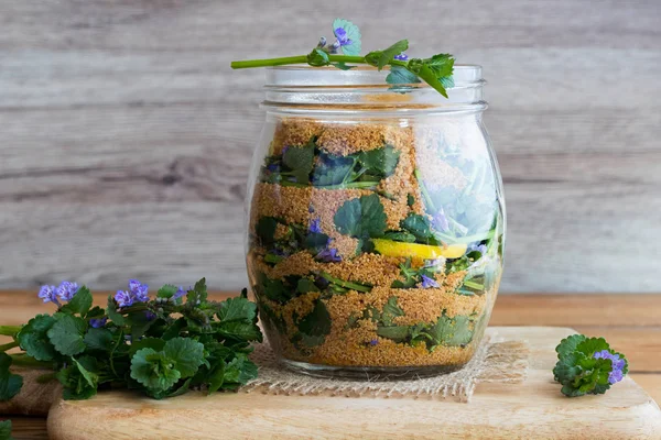 Un vaso di vetro pieno di foglie di edera macinata e fiori, limone e — Foto Stock
