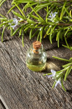 Şeffaf bir yağ şişesi ve taze çiçek açan bir rosema.