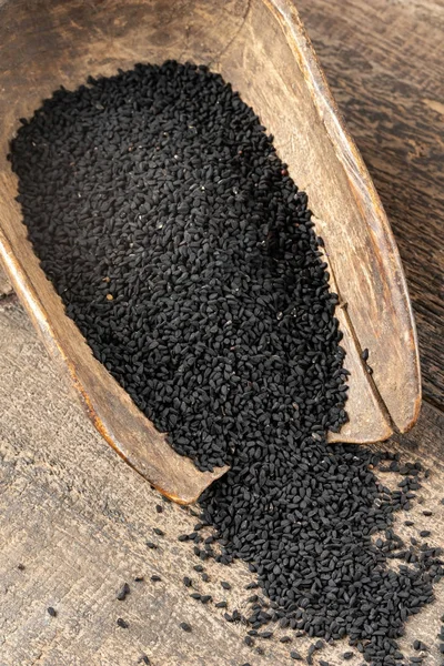 Черные семена тмина, пролитые из винтажного совок — стоковое фото