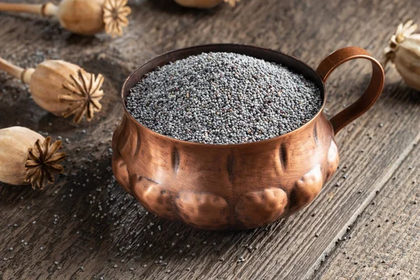 Poppy seeds in a vintage cup, with poppyheads in the background — Stock Photo, Image