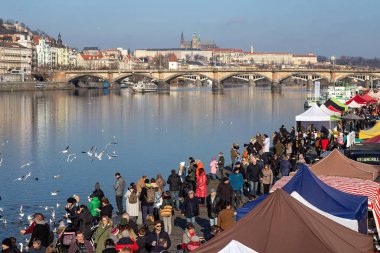 Prag, Çek Cumhuriyeti - 8 Şubat 2020: İnsanlar Naplavka nehir kıyısındaki çiftçi pazarında yürüyorlar, Prag Kalesi ve arka planda köprüler var