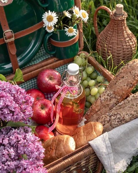 A bottle of water with fruit syrup and other food in a picnic basket, outdoors