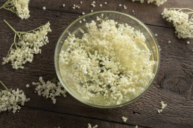 Bitkisel şurup hazırlamak için bir kase suya yaşlı çiçekleri ve limonu ezmek.