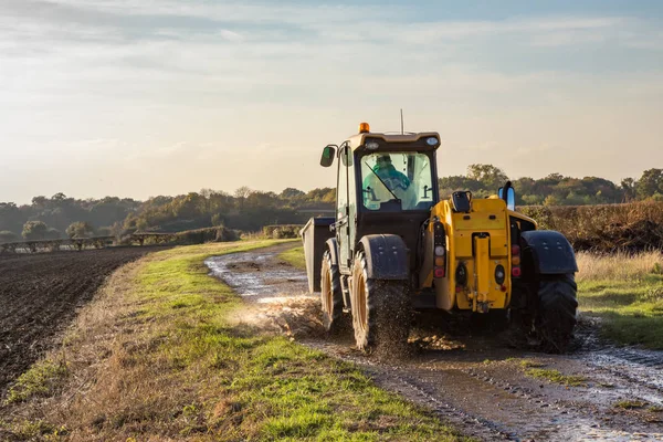 Tractor driving along a wet farm track with a ploughed field to — Stock Photo, Image