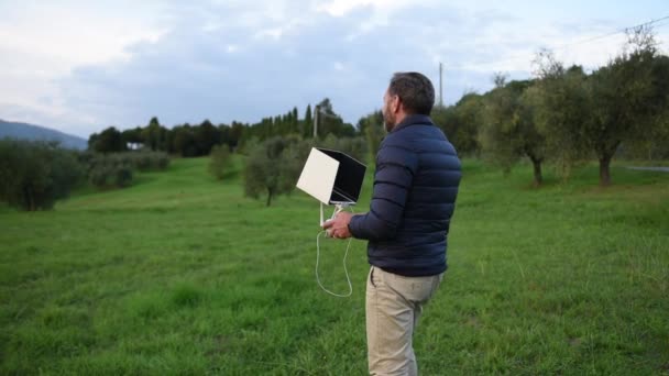 De bebaarde man gekleed in de donsjack maakt zijn drone opstijgen op de landweg — Stockvideo
