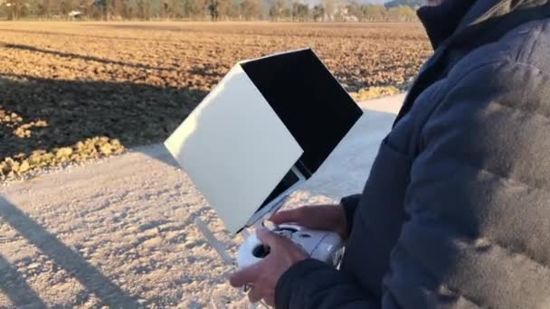 Un hombre barbudo vestido con la chaqueta baja pilota su avión no tripulado en la carretera del campo, al atardecer — Vídeos de Stock