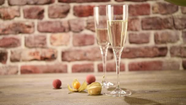 Video of poring champagne into two flutes on the wooden table with the brick background, selective focus — Stock Video