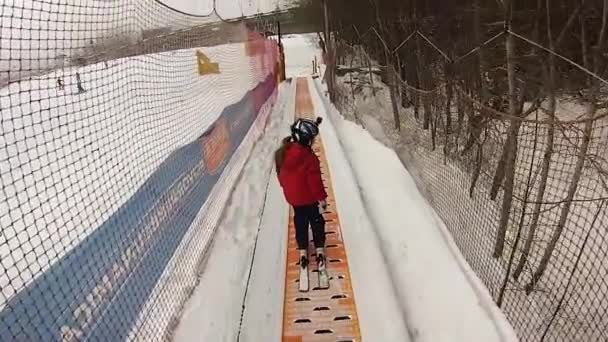 En liten flicka med gopro på hennes hjälm på den tapis nybörjarbacken under hennes första ski-lektion — Stockvideo