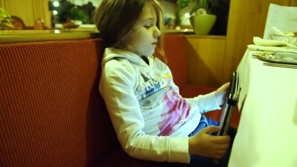 Маленька дівчинка грає зі своїм планшетом у ресторані, 4K — стокове відео