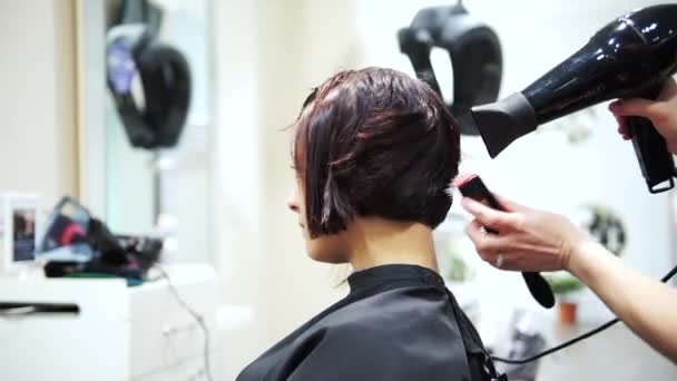 Una joven hermosa mujer secándose el pelo oscuro en los peluqueros, 4K — Vídeo de stock