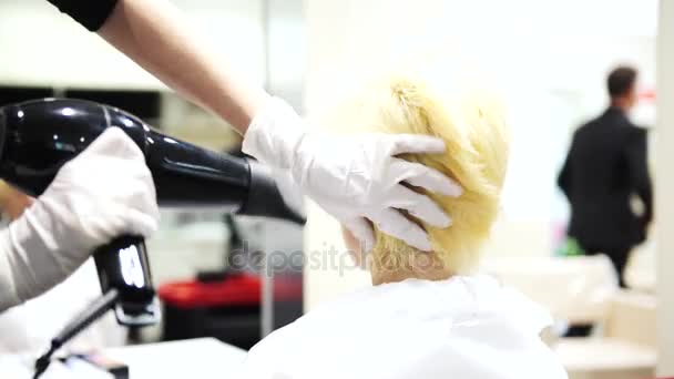 Una joven hermosa mujer secándose el pelo rubio en los peluqueros, 4K — Vídeos de Stock