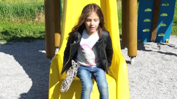 Niña feliz con el pelo castaño largo jugando en el tobogán en el parque, cámara lenta HD — Vídeo de stock