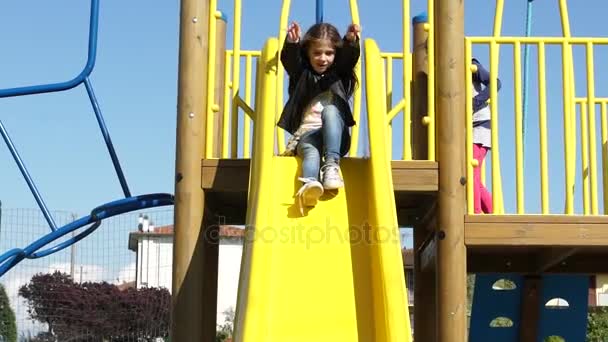 Счастливая маленькая девочка с длинными каштановыми волосами, играющая на горке в парке, замедленного действия HD — стоковое видео