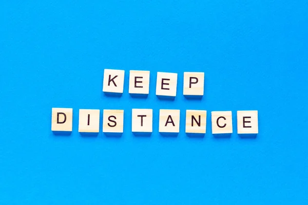 Words keep distance . Wooden inscription on a blue background. Information sign of keep distance from blocks on a blue background. top view, flat layout