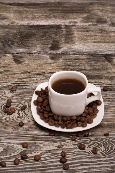 Small white cup of coffee with cocoa beans on wooden background — Stock Photo, Image