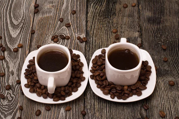 Due piccole tazze bianche di caffè con fagioli di cacao su sfondo di legno — Foto Stock