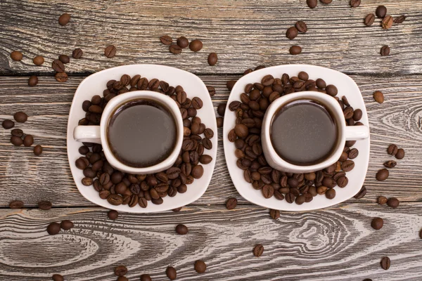 Due piccole tazze bianche di caffè con fagioli di cacao su sfondo di legno — Foto Stock