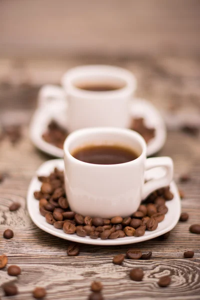 Due piccole tazze bianche di caffè con fagioli di cacao su sfondo di legno — Foto Stock