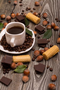 iki küçük beyaz fincan kahve, kurabiye, kakao çekirdekleri, dilim çikolata, fındık ve ahşap zemin üzerine yeşil yaprakları ile