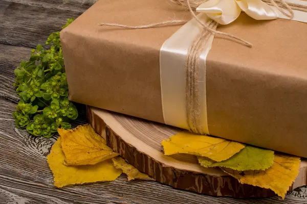 Caja de regalo en el corte del árbol y hojas amarillas sobre fondo de madera —  Fotos de Stock