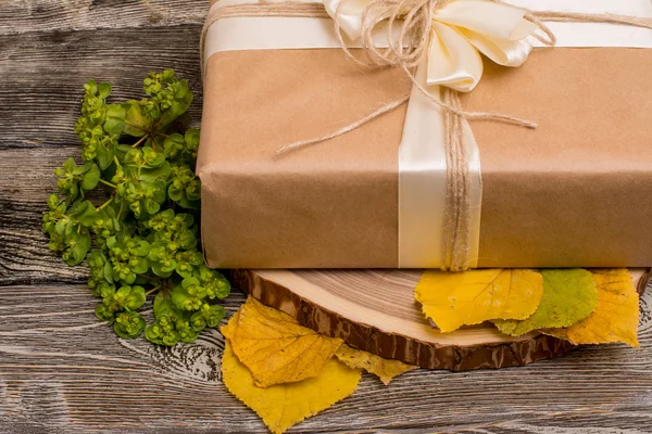 Caja de regalo en el corte del árbol y hojas amarillas sobre fondo de madera —  Fotos de Stock