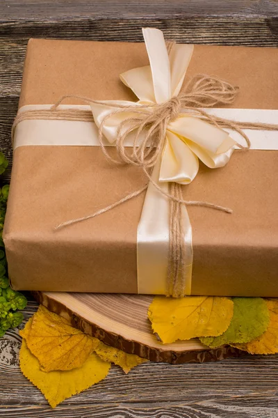 Caja de regalo en el corte del árbol y hojas amarillas sobre fondo de madera —  Fotos de Stock