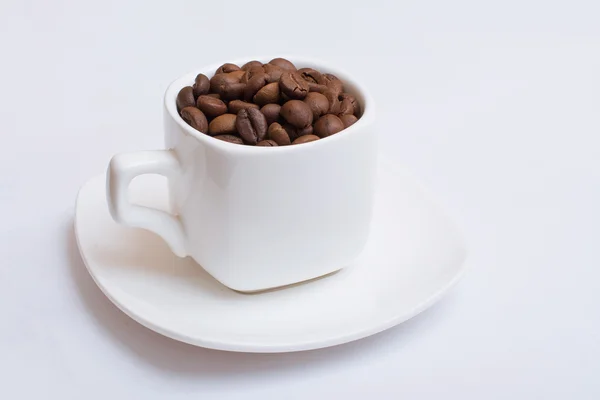 Pequeña taza blanca con granos de café sobre un fondo blanco. Aislado — Foto de Stock