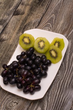 siyah üzüm ve ahşap arka plan beyaz bir tabakta kivi dilimleri