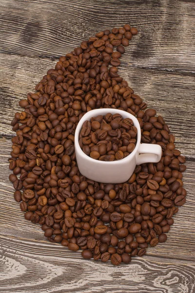 Pequeña taza blanca con granos de café sobre fondo de madera — Foto de Stock