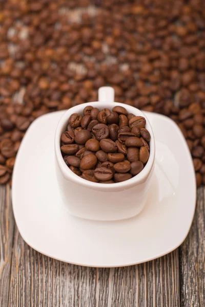 Small white cup with coffee beans on wooden background — Stock Photo, Image
