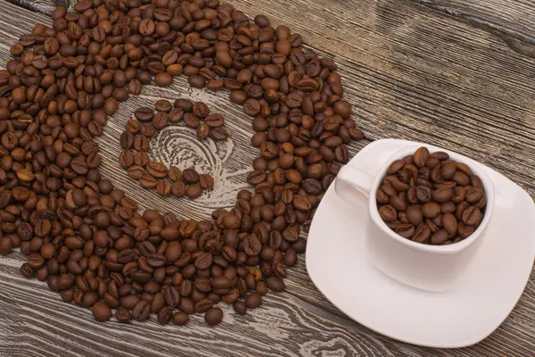 Pequeña taza blanca, la letra c hecha de granos de café sobre fondo de madera — Foto de Stock
