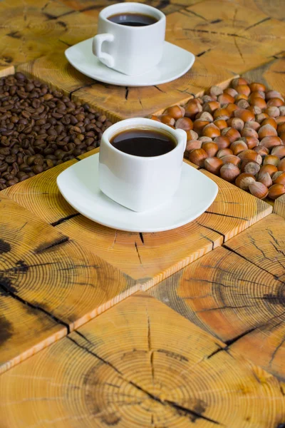 Piccola tazza bianca di caffè, chicchi di caffè torrefatto e nocciole su sfondo di legno da sega legno tagliato — Foto Stock