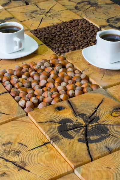 Pequeña taza blanca de café, granos de café tostados y avellanas sobre fondo de madera de madera cortada por sierra — Foto de Stock