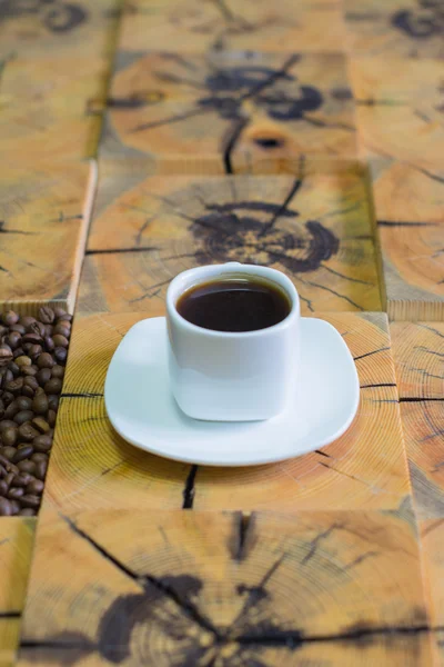 Kleine weiße Tasse Kaffee und geröstete Kaffeebohnen auf Holzgrund aus gesägtem Holz — Stockfoto